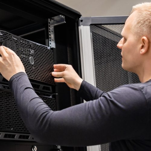 Confident male technician installing servers in enterprise data centre for cloud hosting.